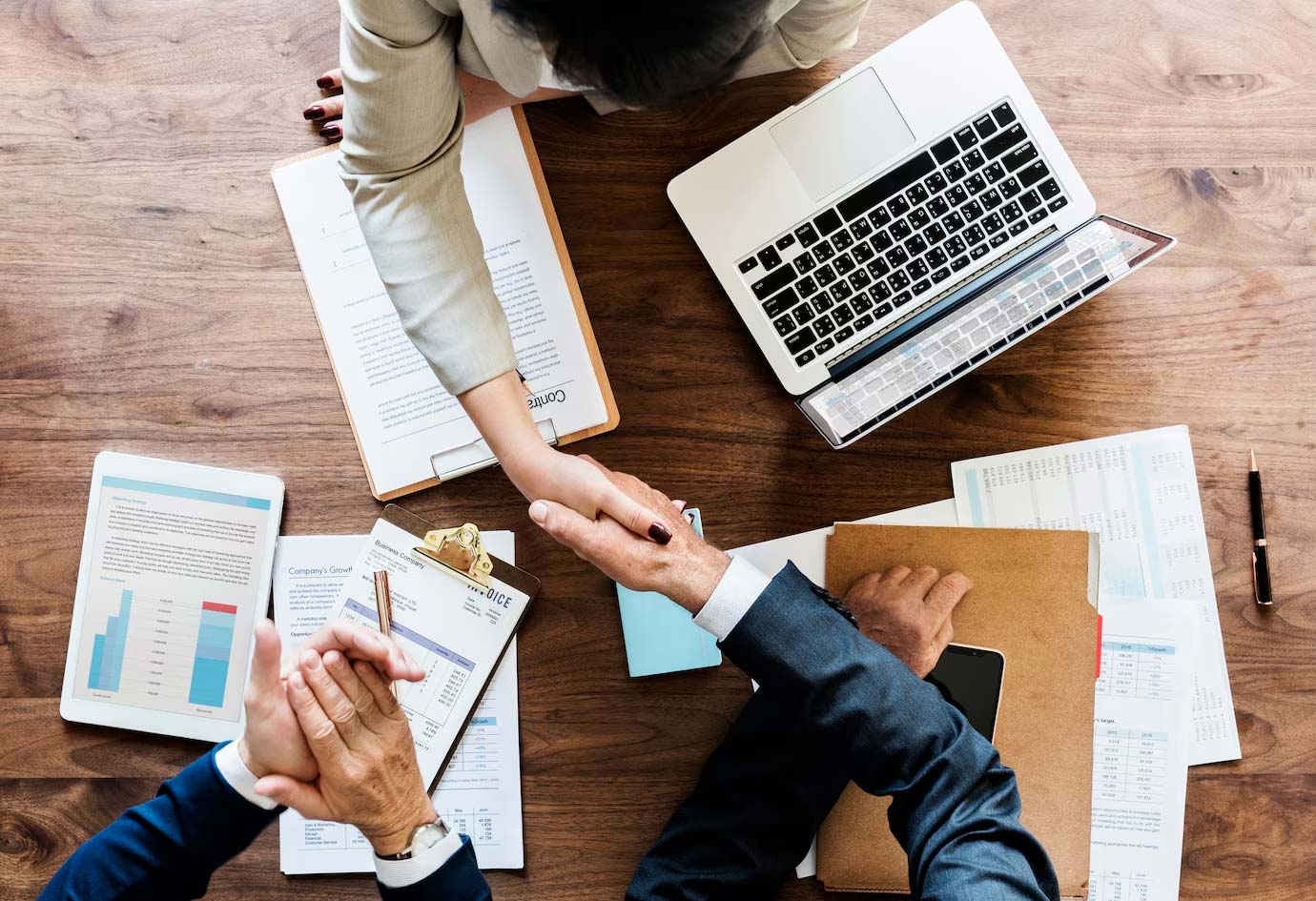 A photo taken from up view. Three business at a table, shaking hands closing a deal.
