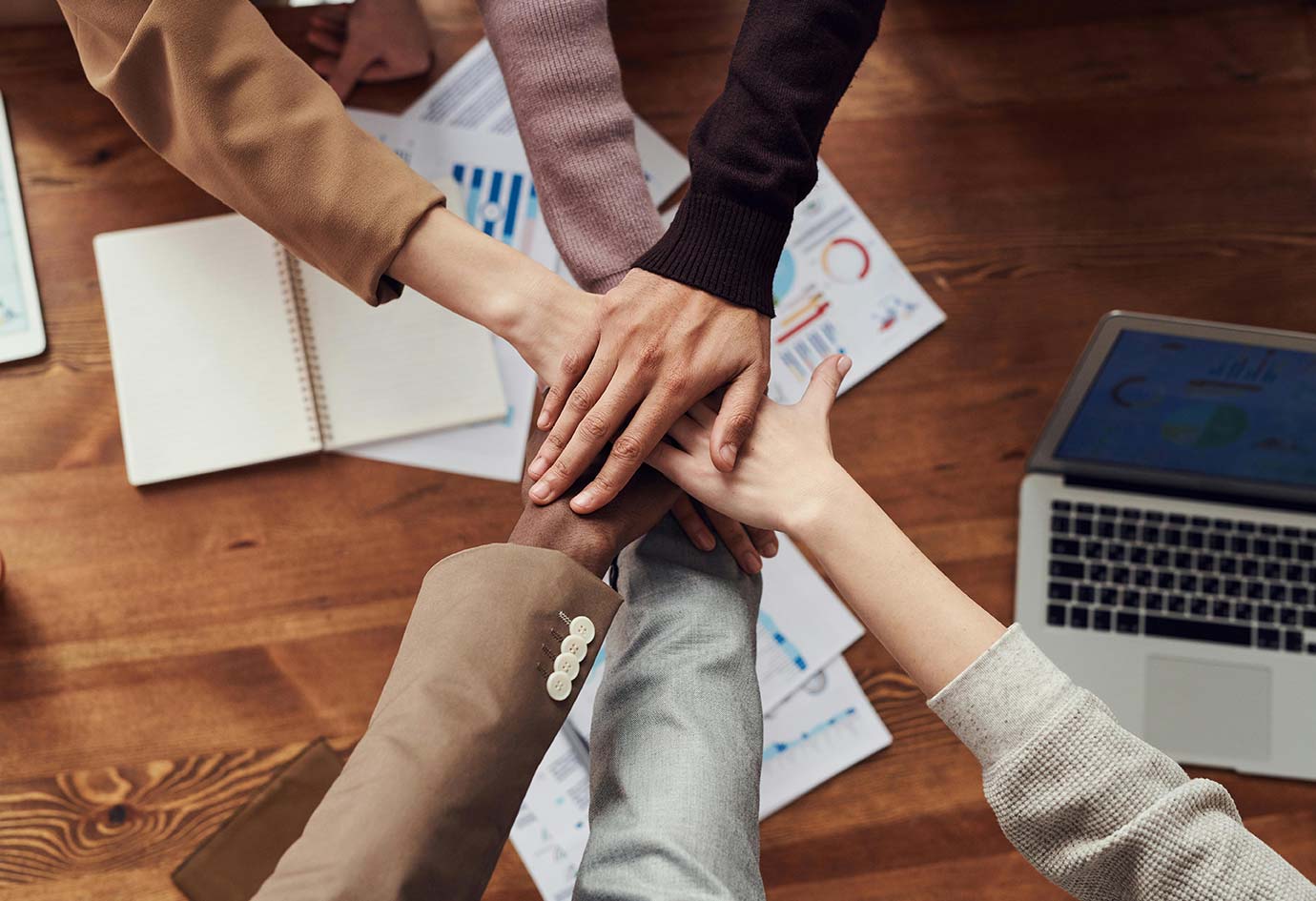a photo of hands united over a table at a business meeting.